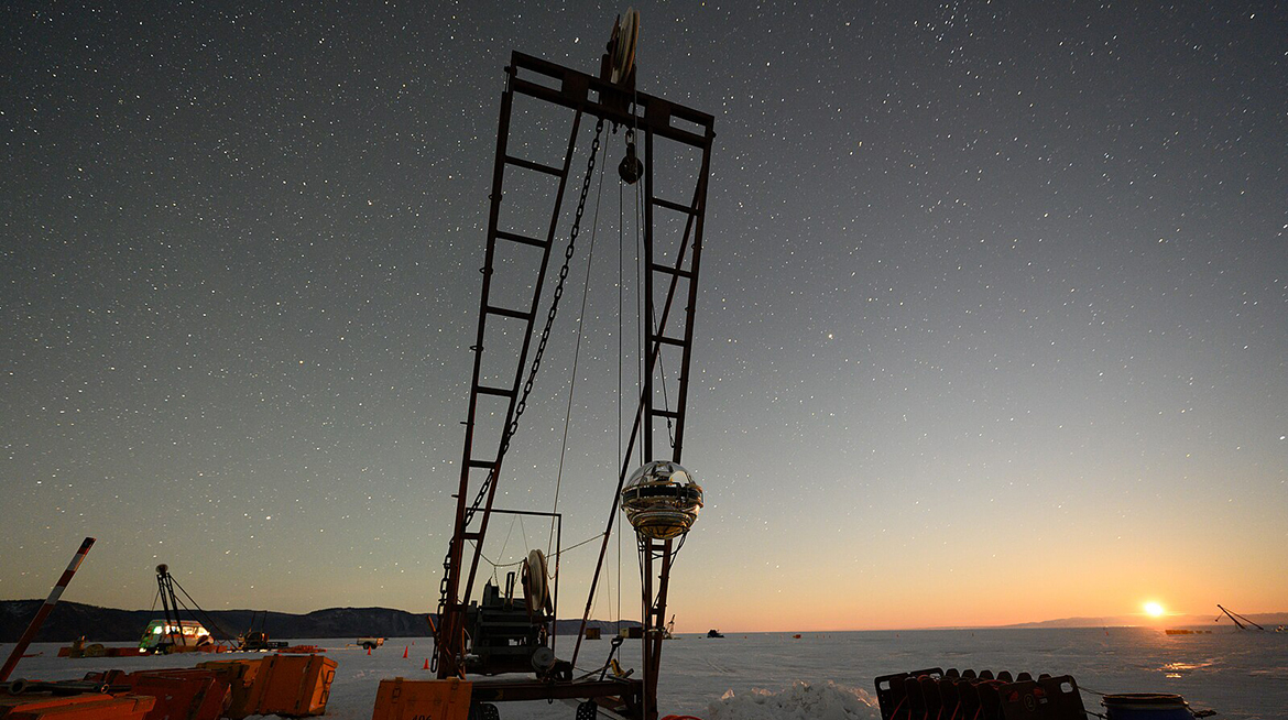 Развертывание нейтринного телескопа Baikal-GVD с ледового покрова озера во время экспедиции на озеро Байкал. В центре: спуско-подъемное устройство и оптический модуль телескопа, готовый к погружению на глубину озера, освещенные восходящей Луной